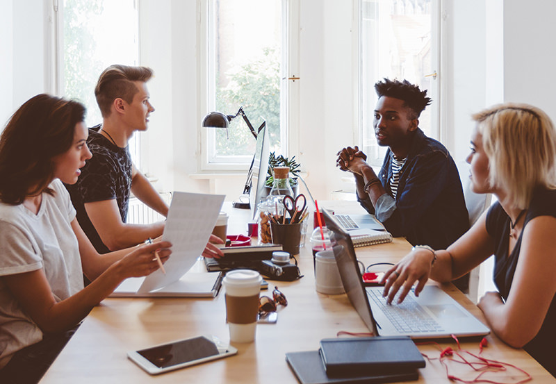 Multi ethnic group of young people sitting at the table and discussing. Creative people co-working in startup office.